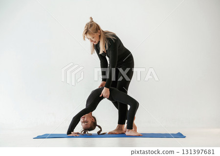 Woman is helping girl. Mother and little daughter are in fitness clothes on yoga mat Woman is helping girl. Mother and little daughter are in fitness clothes on yoga mat 131397681