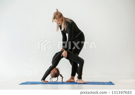 Woman is helping girl. Mother and little daughter are in fitness clothes on yoga mat 131397683
