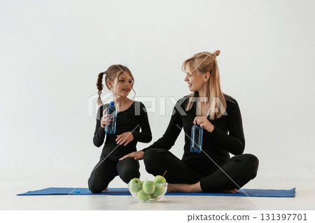 Taking a break, fun, laptop, water and apples. Mother and little daughter are in fitness clothes on yoga mat 131397701