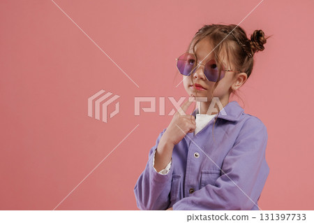 In stylish sunglasses. Cute little girl is against pink background In stylish sunglasses. Cute little girl is against pink background 131397733