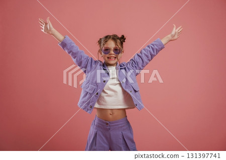Smiling, with hands up and on the sides. Cute little girl is against pink background 131397741