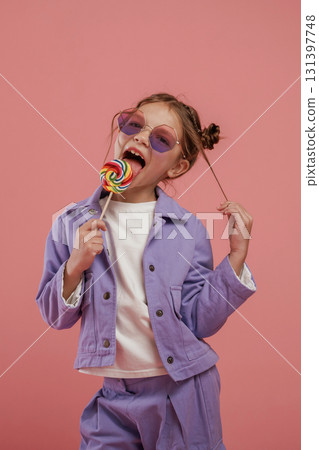 Enjoying sweet candy. Cute little girl is against pink background Enjoying sweet candy. Cute little girl is against pink background 131397748