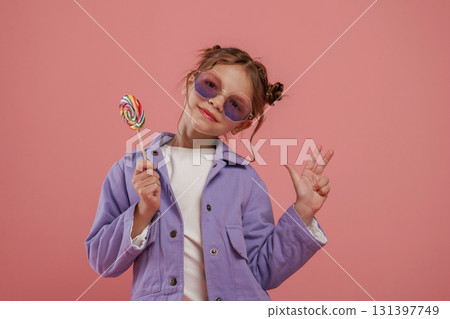 Enjoying sweet candy. Cute little girl is against pink background 131397749