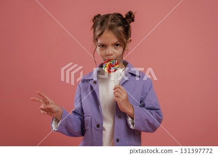 Peace hand gesture, with candy. Cute little girl is against pink background 131397772
