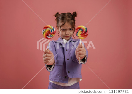 Posing and showing two candies. Cute little girl is against pink background 131397781