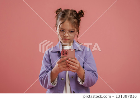 Focused by using smartphone. Cute little girl is against pink background 131397816