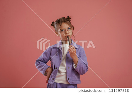 Thinking, holding pen, smart pupil. Cute little girl is against pink background 131397818
