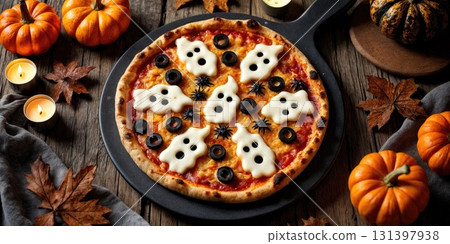 A festive pizza features ghost shapes made from cheese and olives arranged on a wooden table surrounded by pumpkins, leaves, and candles for Halloween. 131397938