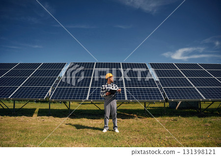 Black notepad in hands. Engineer with photovoltaic solar panels outdoors at daytime Black notepad in hands. Engineer with photovoltaic solar panels outdoors at daytime 131398121