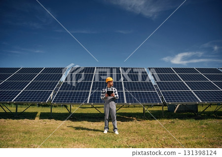 Black notepad in hands. Engineer with photovoltaic solar panels outdoors at daytime 131398124