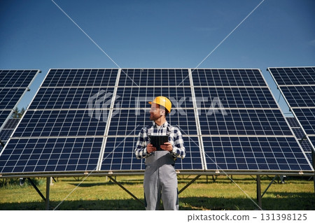 Black notepad in hands. Engineer with photovoltaic solar panels outdoors at daytime 131398125