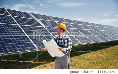 Big paper with plan, reading. Engineer with photovoltaic solar panels outdoors at daytime Big paper with plan, reading. Engineer with photovoltaic solar panels outdoors at daytime 131398129