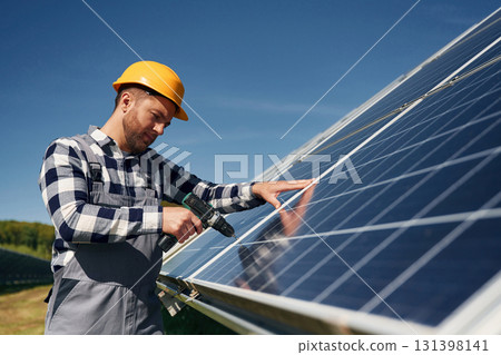 Almost done, installation by using drill. Engineer with photovoltaic solar panels outdoors at daytime 131398141