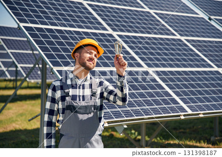 Traditional light bulb in hand. Engineer with photovoltaic solar panels outdoors at daytime Traditional light bulb in hand. Engineer with photovoltaic solar panels outdoors at daytime 131398187