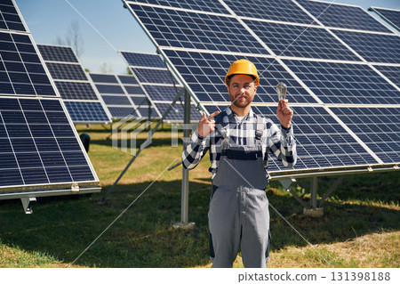 Traditional light bulb in hand. Engineer with photovoltaic solar panels outdoors at daytime Traditional light bulb in hand. Engineer with photovoltaic solar panels outdoors at daytime 131398188