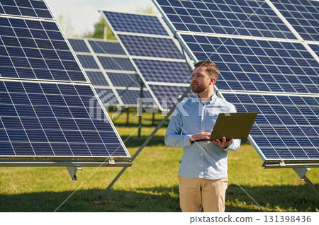Holding laptop. Engineer with photovoltaic solar panels outdoors at daytime Holding laptop. Engineer with photovoltaic solar panels outdoors at daytime 131398436