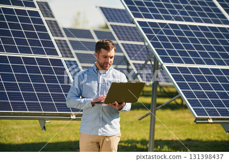 Holding laptop. Engineer with photovoltaic solar panels outdoors at daytime 131398437