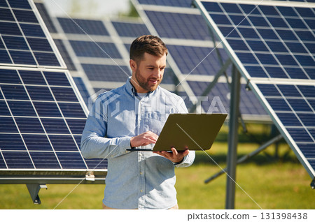 Holding laptop. Engineer with photovoltaic solar panels outdoors at daytime 131398438