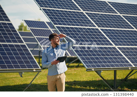 Holding laptop. Engineer with photovoltaic solar panels outdoors at daytime 131398440