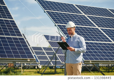 Using walkie talkie and holding notepad. Engineer with photovoltaic solar panels outdoors at daytime Using walkie talkie and holding notepad. Engineer with photovoltaic solar panels outdoors at daytime 131398445