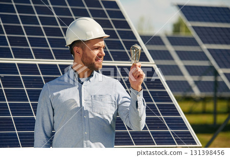 Bulb in hand. Engineer with photovoltaic solar panels outdoors at daytime Bulb in hand. Engineer with photovoltaic solar panels outdoors at daytime 131398456