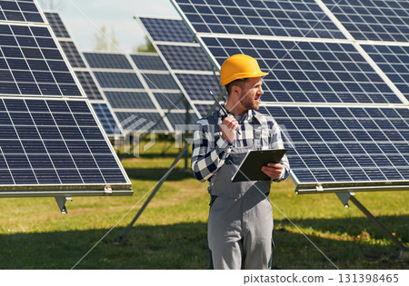 Communication by using walkie talkie. Engineer with photovoltaic solar panels outdoors at daytime Communication by using walkie talkie. Engineer with photovoltaic solar panels outdoors at daytime 131398465