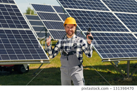 Drill in hand. Engineer with photovoltaic solar panels outdoors at daytime 131398470