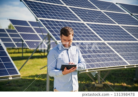 Digital tablet in hand. Engineer with photovoltaic solar panels outdoors at daytime Digital tablet in hand. Engineer with photovoltaic solar panels outdoors at daytime 131398478