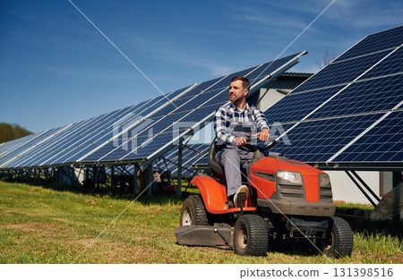 Red lawnmower. Engineer with photovoltaic solar panels outdoors at daytime 131398516