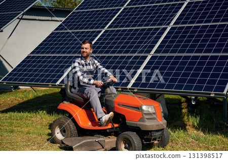 Red lawnmower. Engineer with photovoltaic solar panels outdoors at daytime 131398517