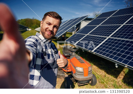 Red lawnmower. Engineer with photovoltaic solar panels outdoors at daytime 131398520