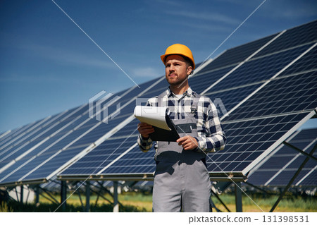 On the field with notepad in hands. Engineer with photovoltaic solar panels outdoors at daytime On the field with notepad in hands. Engineer with photovoltaic solar panels outdoors at daytime 131398531