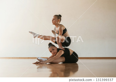 On the back of other girl, standing on hands. Kids are doing athletic exercises indoors together 131399337