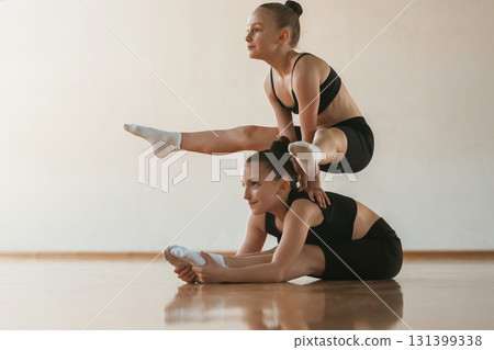 On the back of other girl, standing on hands. Kids are doing athletic exercises indoors together 131399338