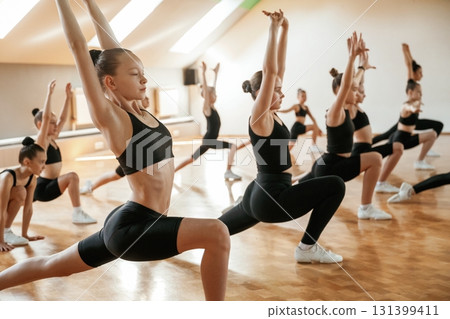 Vitality and flexibility conception. Group of female kids practicing athletic exercises together indoors Vitality and flexibility conception. Group of female kids practicing athletic exercises together indoors 131399411