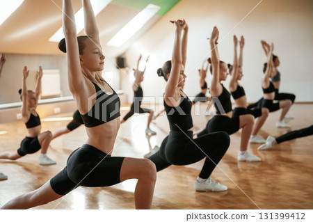 Vitality and flexibility conception. Group of female kids practicing athletic exercises together indoors Vitality and flexibility conception. Group of female kids practicing athletic exercises together indoors 131399412