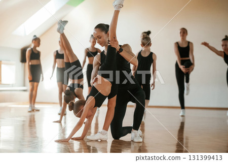 Trainer is helping girl. Group of female kids practicing athletic exercises together indoors 131399413