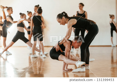 Friendly coach is helping. Group of female kids practicing athletic exercises together indoors Friendly coach is helping. Group of female kids practicing athletic exercises together indoors 131399453