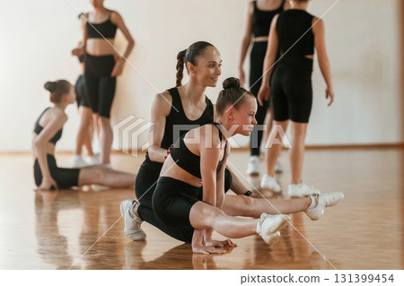 Friendly coach is helping. Group of female kids practicing athletic exercises together indoors 131399454