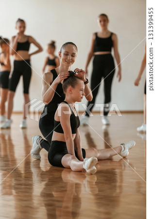 Friendly coach is helping. Group of female kids practicing athletic exercises together indoors 131399455