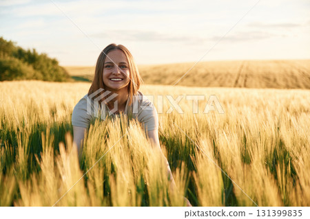 Sitting and smiling. Young woman is on the beautiful agricultural field at daytime 131399835