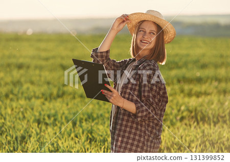 Positive mood, with straw hat and with documents. Young woman is on the beautiful agricultural field at daytime Positive mood, with straw hat and with documents. Young woman is on the beautiful agricultural field at daytime 131399852