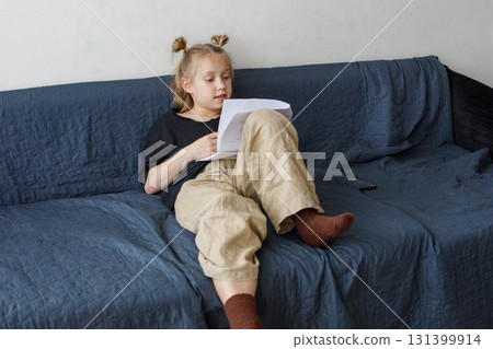 Happy little girl sitting on sofa reading book at home. Childhood and people concept Happy little girl sitting on sofa reading book at home. Childhood and people concept 131399914
