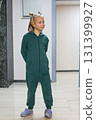 Cheerful little girl wearing green jumpsuit standing in lobby lounge. Adorable child 6 years old 131399927