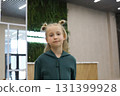 Blond little girl wearing green jumpsuit standing in lobby lounge. Adorable child 6 years old 131399928