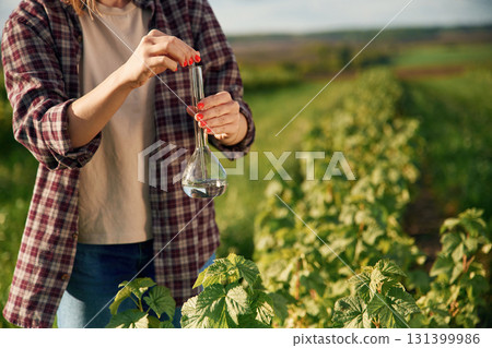 With test tube, doing research. Young woman is on the beautiful agricultural field at daytime With test tube, doing research. Young woman is on the beautiful agricultural field at daytime 131399986