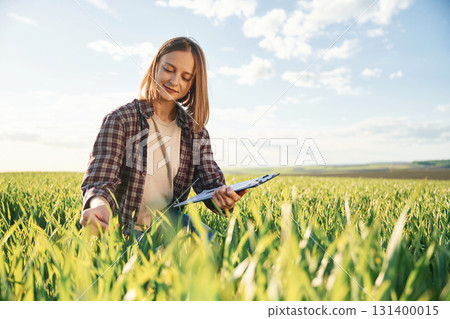 Touching the plant. Young woman is on the beautiful agricultural field at daytime Touching the plant. Young woman is on the beautiful agricultural field at daytime 131400015