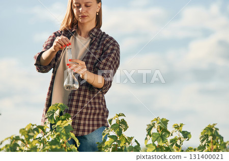 Working by using test tube. Young woman is on the beautiful agricultural field at daytime 131400021