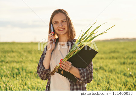 Using smartphone. Young woman is on the beautiful agricultural field at daytime 131400033