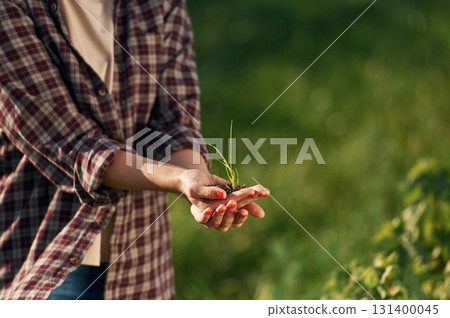 Close up view of soil and plant in hands. Young woman is on the beautiful agricultural field at daytime Close up view of soil and plant in hands. Young woman is on the beautiful agricultural field at daytime 131400045